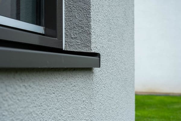 Antraciet aluminium vensterbank met kopschotten onder een raam in een gestucte crepi-gevel